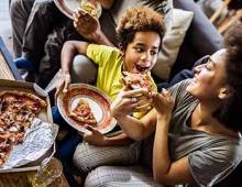 Mom feeding her son a slice of pizza